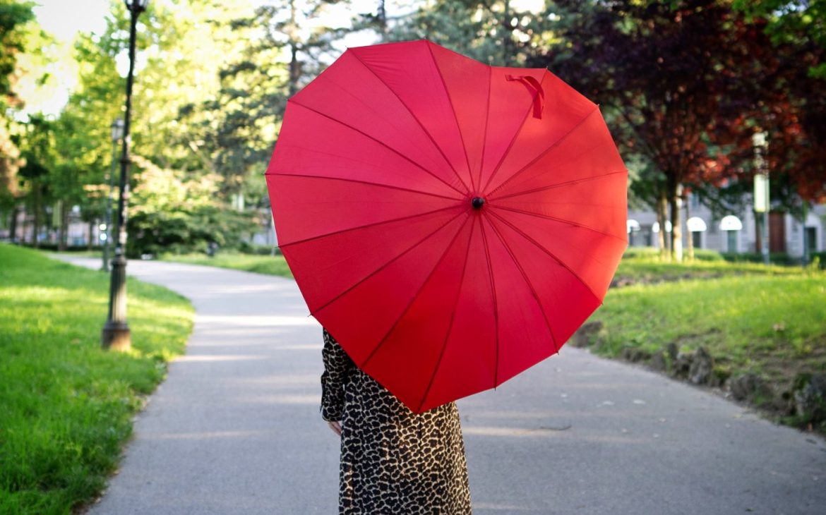 Marie Biondini modella over 50 e fashion blogger di schiena nel parco con abito animalier e ombrello rosso a forma di cuore