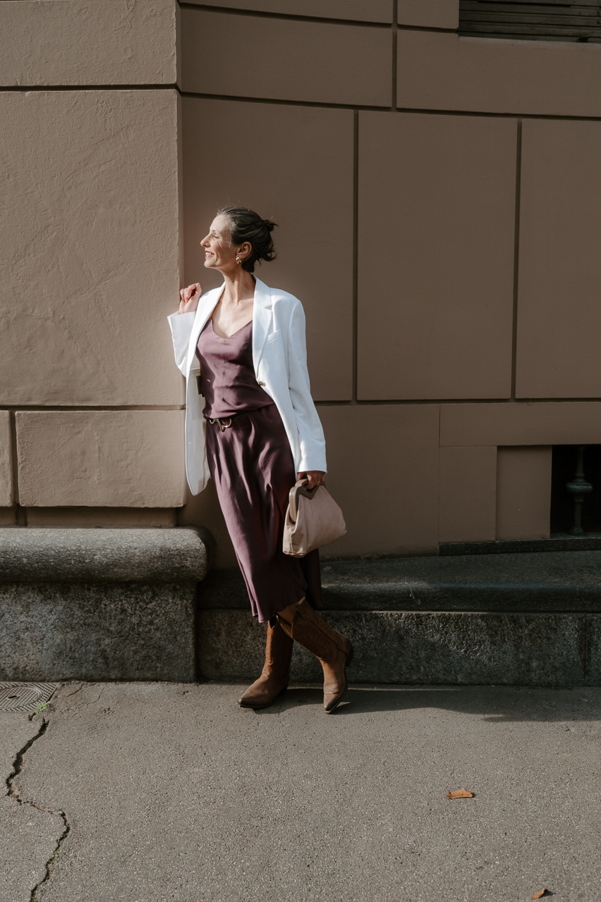 Marie Biondini modella over 50 indossa look country chic giacca blazer bianca primavera over, slipdress, texani
